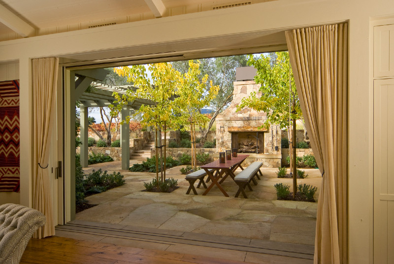 Foto di un grande patio o portico country dietro casa con un focolare, pavimentazioni in pietra naturale e una pergola