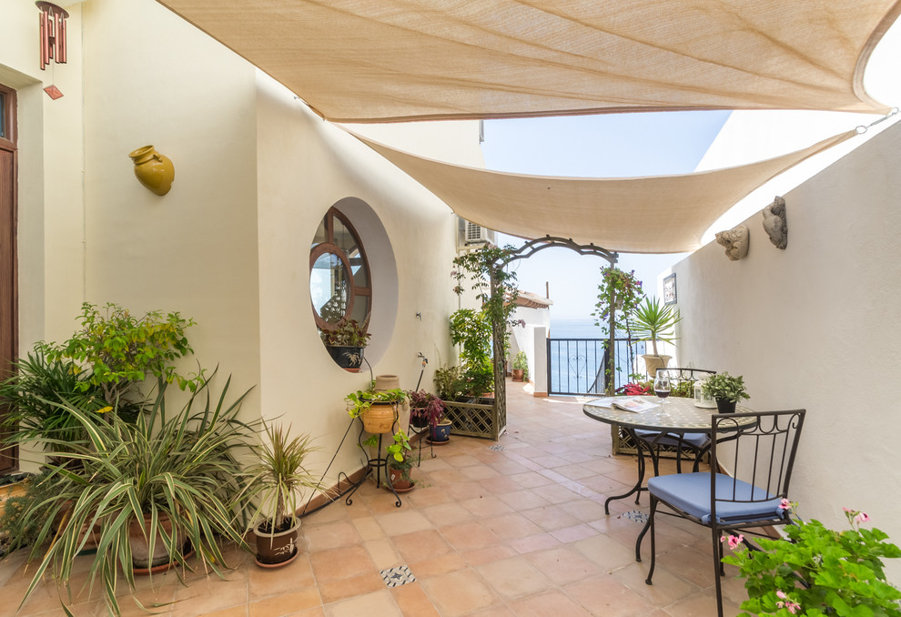 Ejemplo de patio mediterráneo con jardín de macetas, suelo de baldosas y toldo