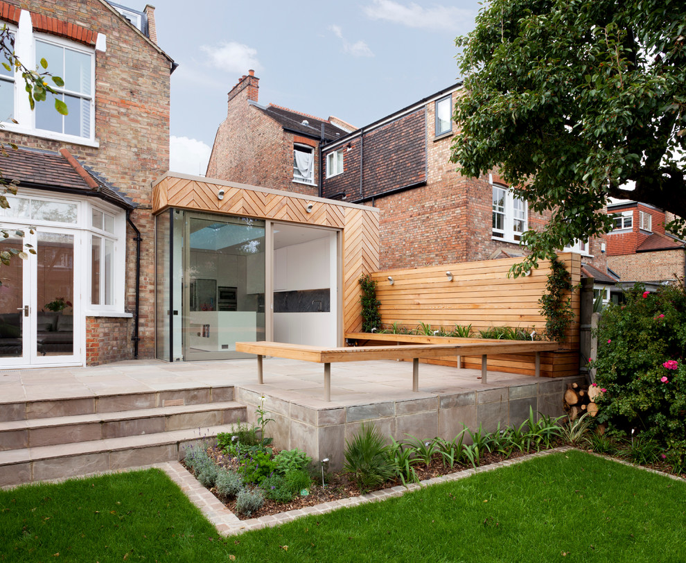 Large contemporary back patio in London with natural stone paving and no cover.