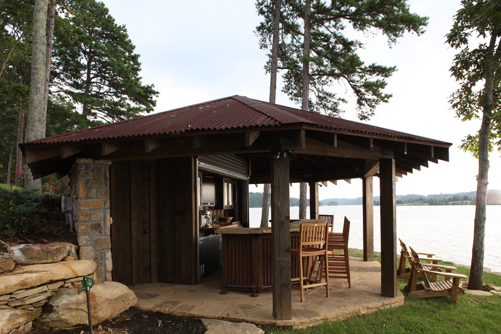 Réalisation d'une grande terrasse arrière chalet avec une cuisine d'été, des pavés en pierre naturelle et un gazebo ou pavillon.