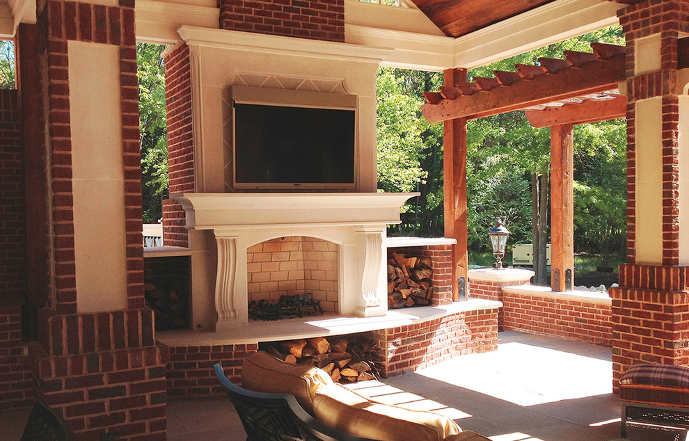 Aménagement d'une grande terrasse arrière classique avec des pavés en pierre naturelle, une extension de toiture et un foyer extérieur.