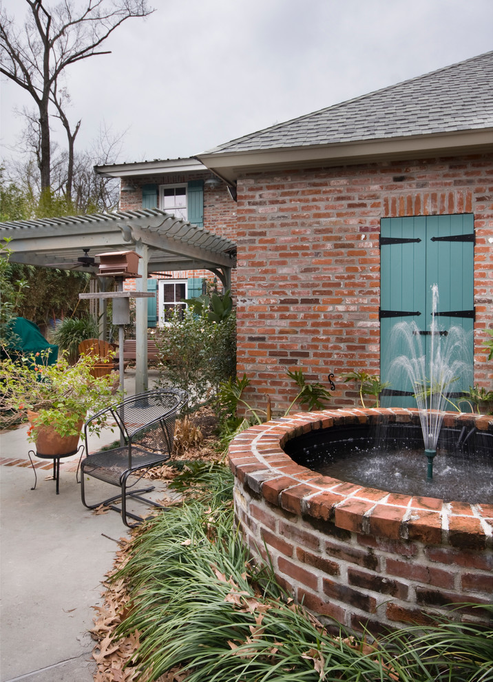 Immagine di un ampio patio o portico chic in cortile con fontane, lastre di cemento e una pergola