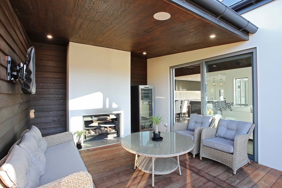 Idées déco pour une terrasse en bois moderne de taille moyenne avec une cheminée, une cour et une extension de toiture.