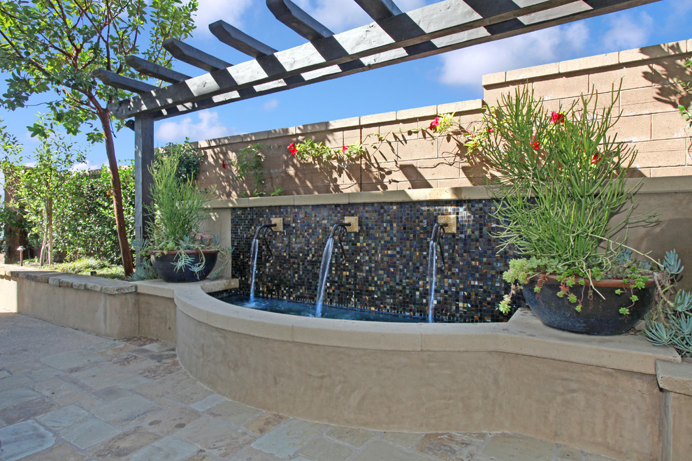 This is an example of a small mediterranean side patio in Orange County with a water feature, natural stone paving and a pergola.