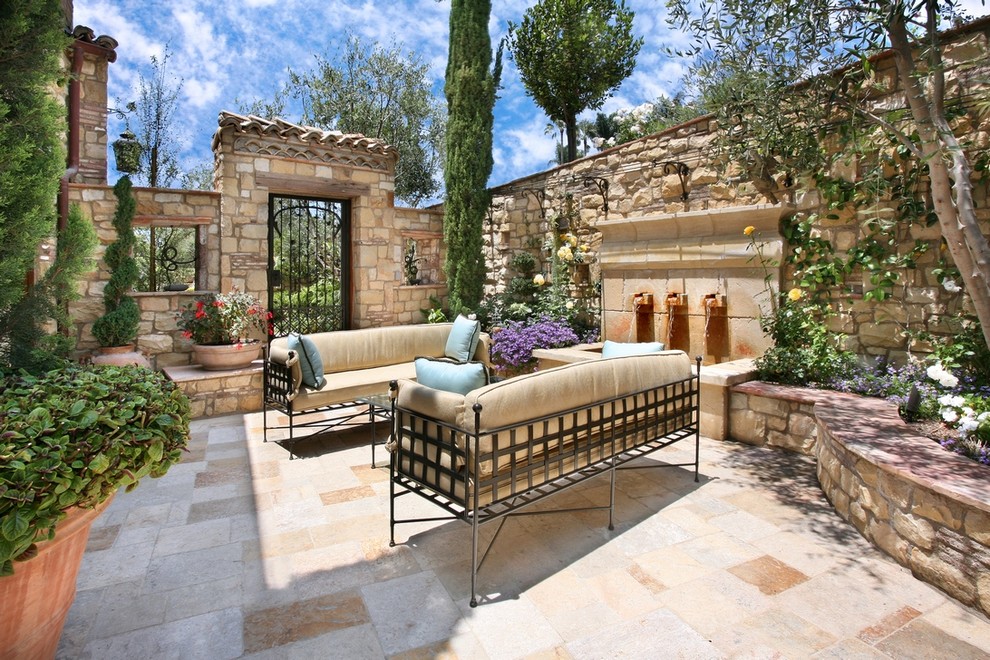 This is an example of a medium sized mediterranean side patio in Orange County with a water feature, tiled flooring and no cover.