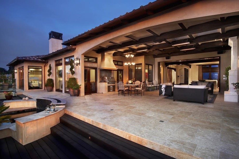 Immagine di un grande patio o portico mediterraneo dietro casa con un focolare, pavimentazioni in pietra naturale e un tetto a sbalzo