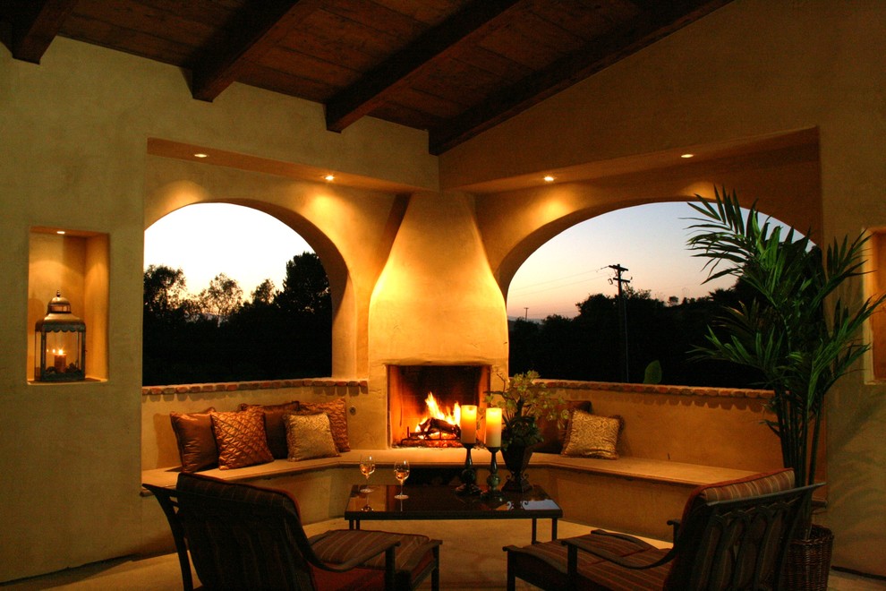 Cette image montre une terrasse arrière méditerranéenne avec un foyer extérieur, des pavés en pierre naturelle et une extension de toiture.