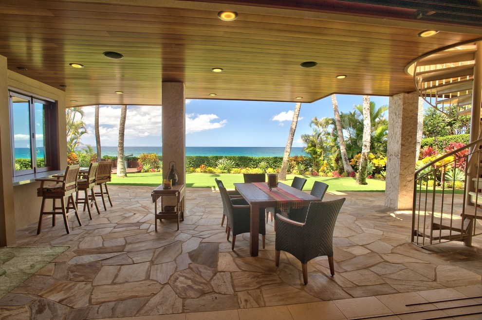 ハワイにある巨大なトロピカルスタイルのおしゃれな裏庭のテラス (天然石敷き、張り出し屋根) の写真