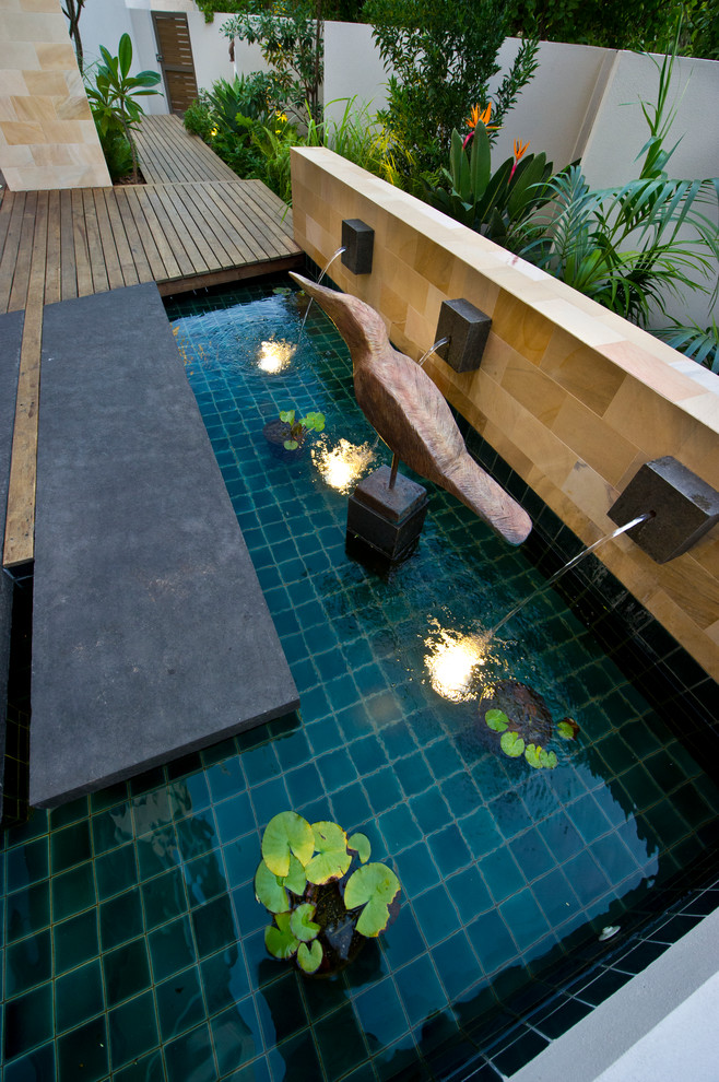 Réalisation d'une petite terrasse avant design avec un point d'eau et des pavés en pierre naturelle.