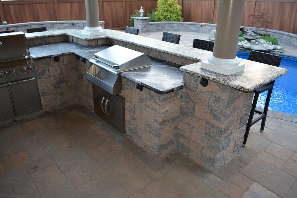 Example of a large classic backyard brick patio kitchen design in New York with a pergola