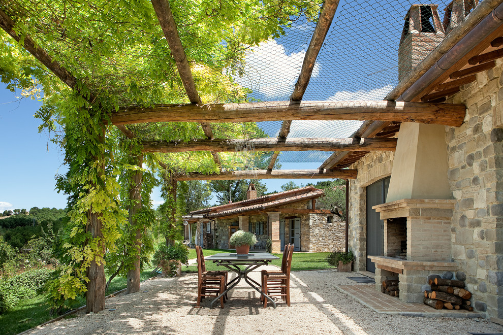Immagine di un patio o portico mediterraneo con una pergola, ghiaia e un caminetto