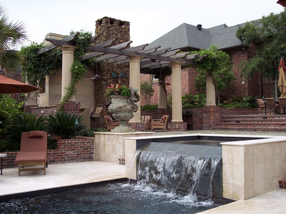 Example of a large island style backyard stone patio fountain design in New Orleans with a pergola
