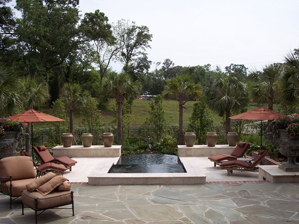 Example of a large island style backyard stone patio fountain design in New Orleans with a pergola