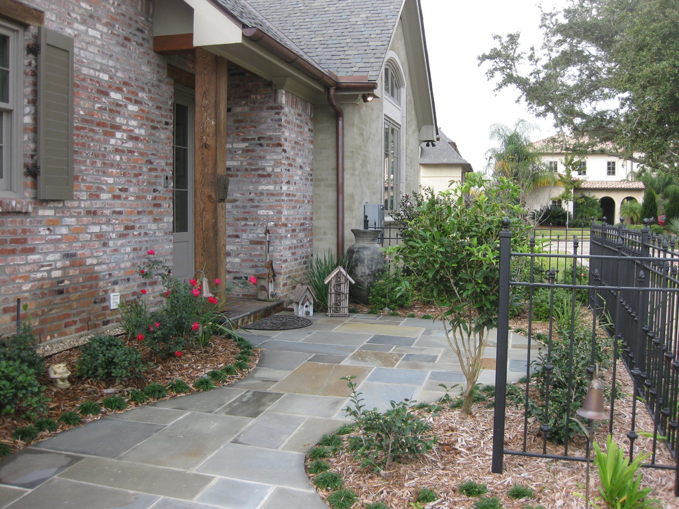Patio - small rustic front yard stone patio idea in New Orleans with a roof extension