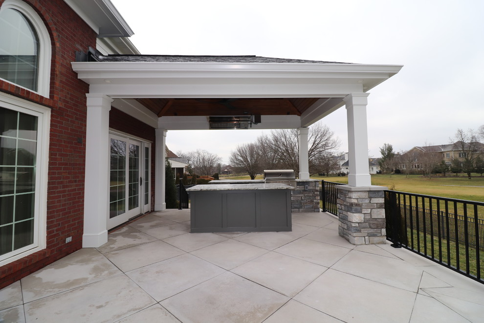Cette photo montre une grande terrasse arrière chic avec une cuisine d'été, des pavés en béton et une extension de toiture.