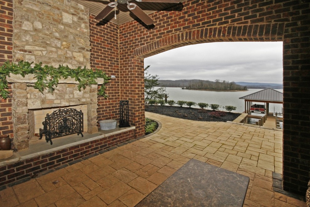 Cette image montre une grande terrasse arrière craftsman avec un foyer extérieur, des pavés en pierre naturelle et une extension de toiture.