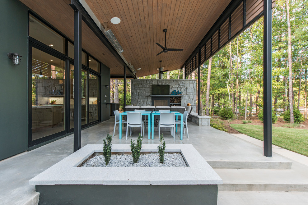 Foto di un grande patio o portico minimal dietro casa con un caminetto, lastre di cemento e un tetto a sbalzo