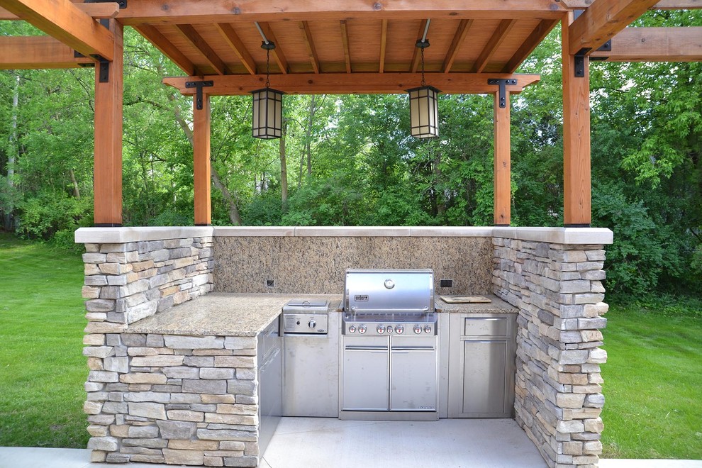This is an example of a large rustic back patio in Milwaukee with an outdoor kitchen, concrete slabs and a pergola.