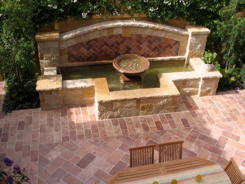 Imagen de patio mediterráneo grande sin cubierta en patio trasero con fuente y adoquines de ladrillo