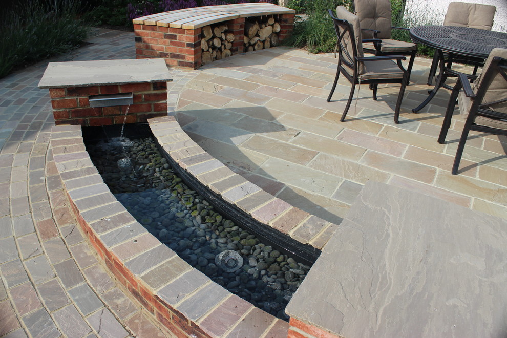 Photo of a medium sized romantic back patio in Hertfordshire with a water feature and natural stone paving.