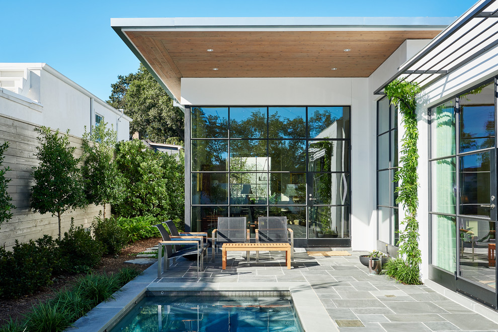This is an example of a large contemporary back patio in Houston with natural stone paving and a roof extension.