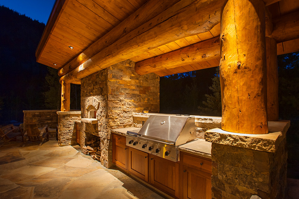 Réalisation d'une terrasse latérale chalet avec une cuisine d'été et des pavés en pierre naturelle.