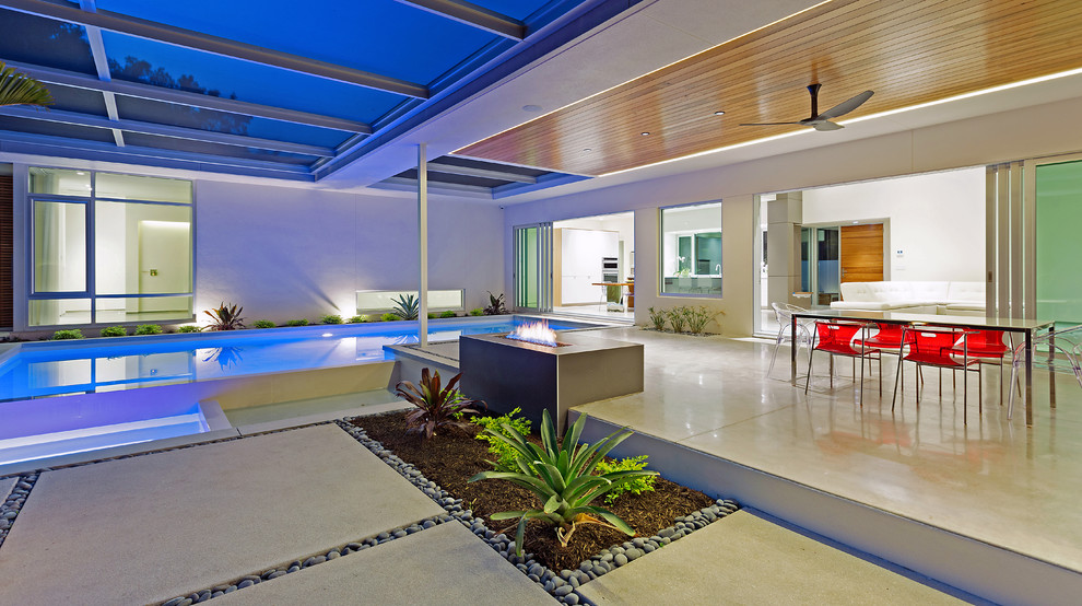 Cette photo montre une grande terrasse arrière tendance avec un foyer extérieur, une dalle de béton et une extension de toiture.