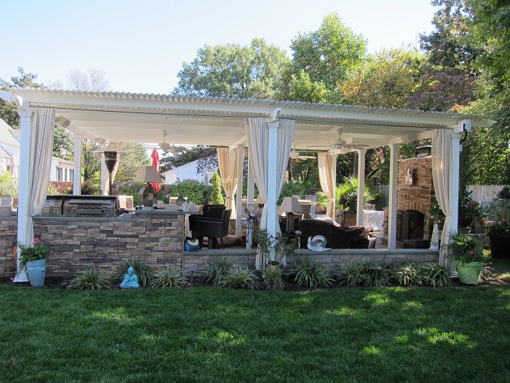 Cette image montre une terrasse arrière traditionnelle de taille moyenne avec des pavés en pierre naturelle, une pergola et une cuisine d'été.