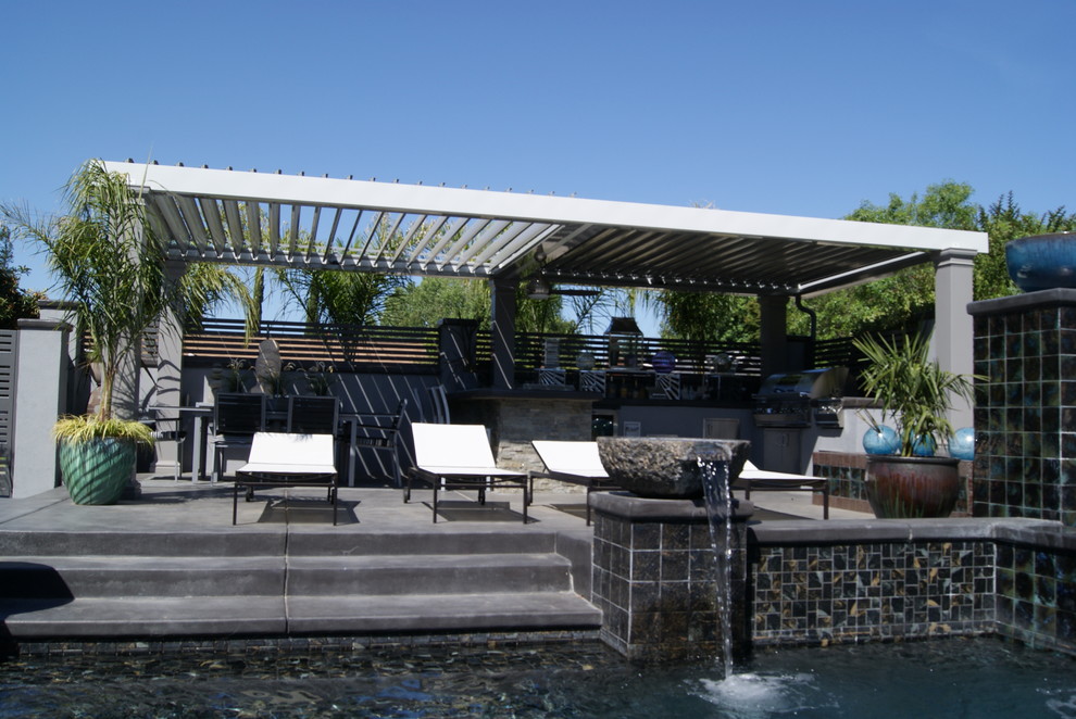 Esempio di un grande patio o portico tropicale dietro casa con fontane, lastre di cemento e una pergola