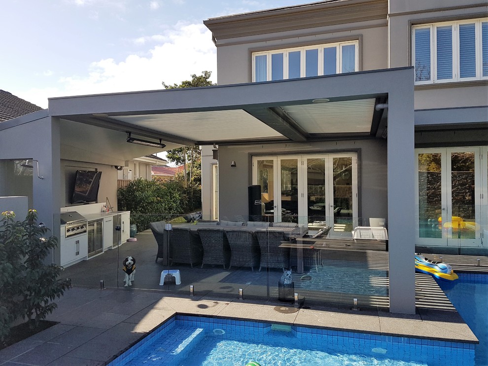 This is an example of a large contemporary back patio in Melbourne with an outdoor kitchen, a roof extension and natural stone paving.