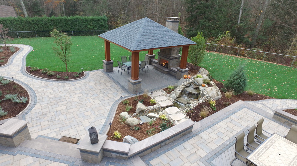 Large mountain style backyard concrete paver patio photo in New York with a fire pit and a gazebo