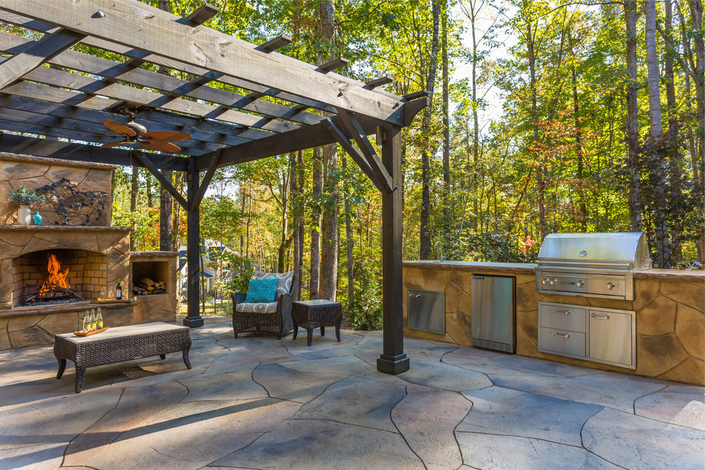 Example of a large minimalist backyard stamped concrete patio kitchen design in Raleigh with a pergola