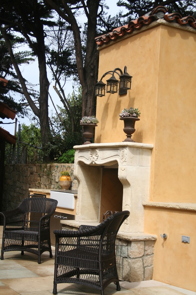 Bild på en liten medelhavsstil uteplats på baksidan av huset, med en öppen spis och naturstensplattor