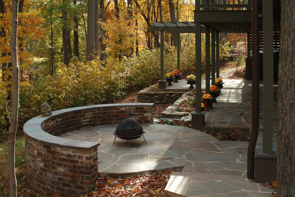 Cette image montre une terrasse chalet avec un foyer extérieur, des pavés en pierre naturelle et une pergola.
