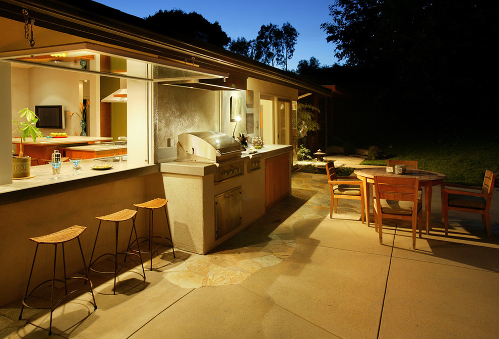 Large contemporary back patio in Orange County with an outdoor kitchen, natural stone paving and an awning.