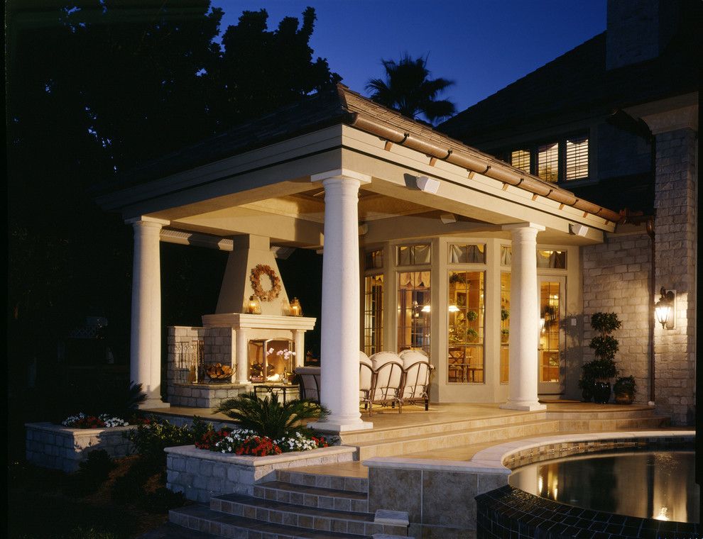 Immagine di un grande patio o portico chic dietro casa con un focolare, pavimentazioni in pietra naturale e un tetto a sbalzo