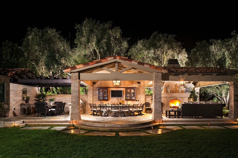 Inspiration for an expansive mediterranean back patio in Orange County with an outdoor kitchen, natural stone paving and an awning.