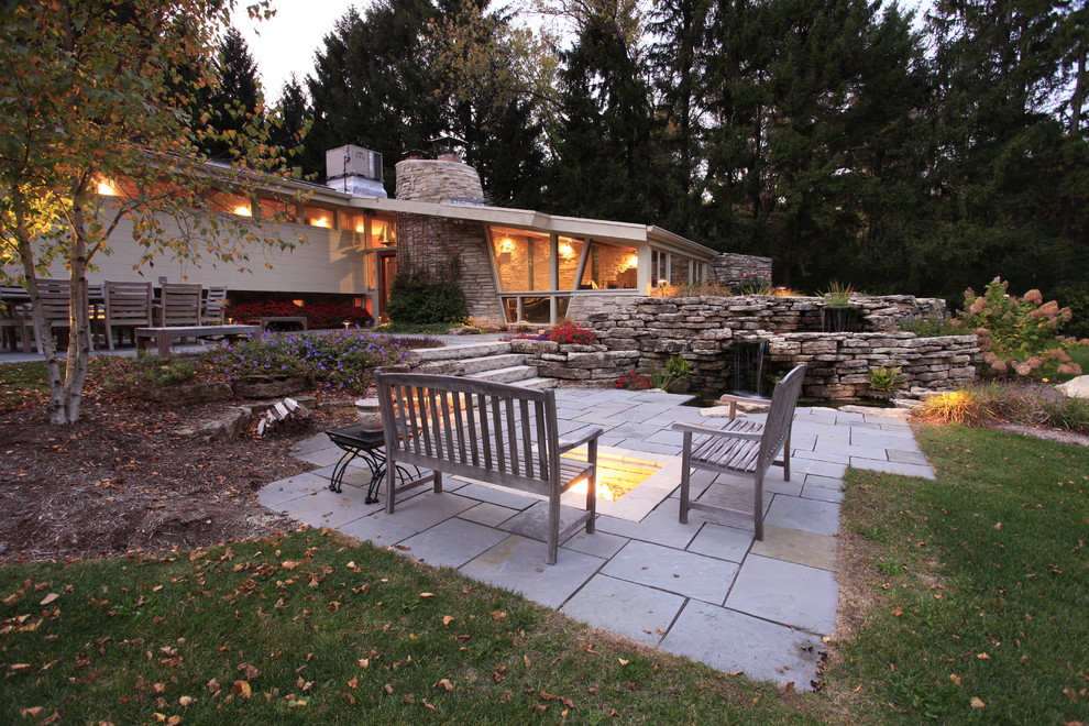 Foto di un grande patio o portico minimal dietro casa con pavimentazioni in pietra naturale, nessuna copertura e un focolare