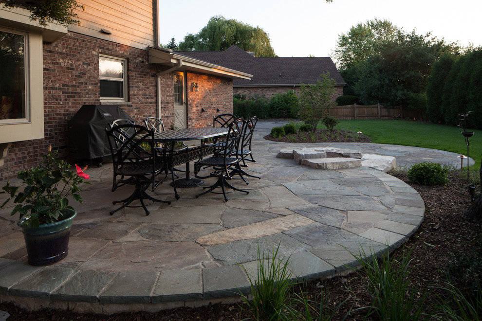 This is an example of a medium sized classic back patio in Milwaukee with a fire feature, natural stone paving and no cover.