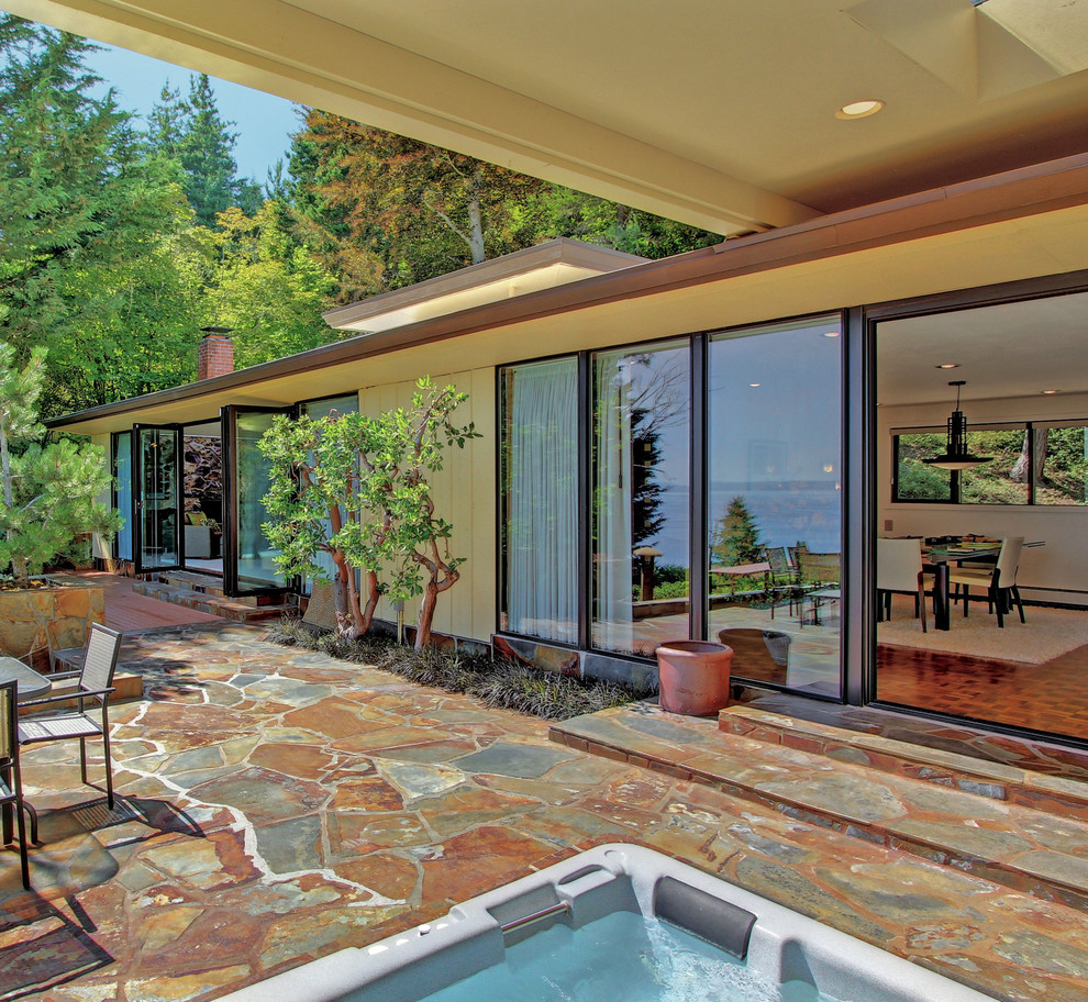 Design ideas for a midcentury patio in Seattle with natural stone paving and a roof extension.