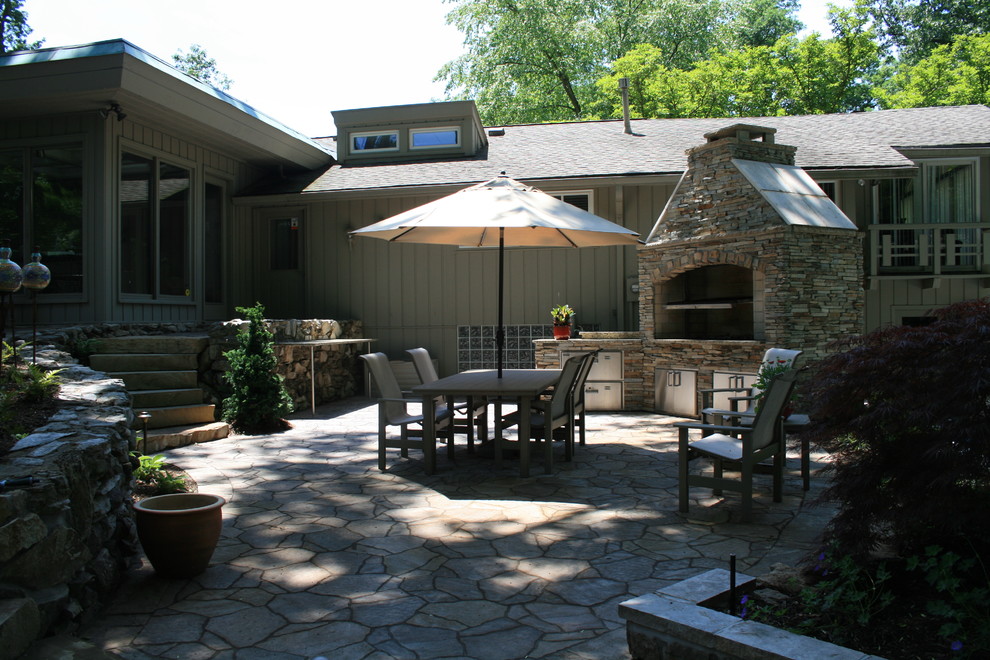 This is an example of a large midcentury back patio in St Louis with an outdoor kitchen, natural stone paving and no cover.