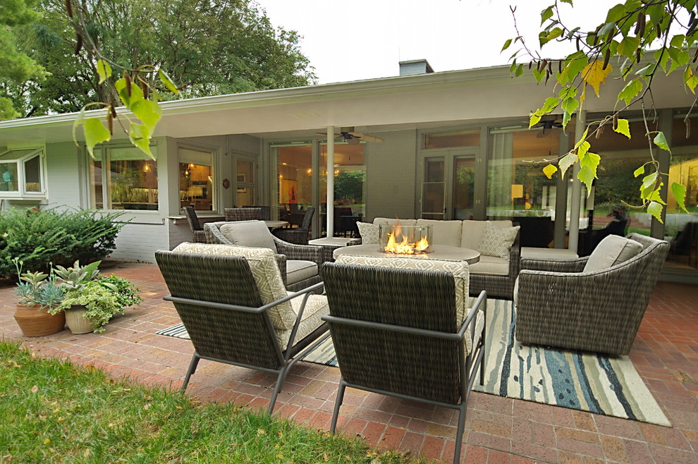 Example of a large mid-century modern backyard brick patio design in Omaha with a fire pit and a roof extension