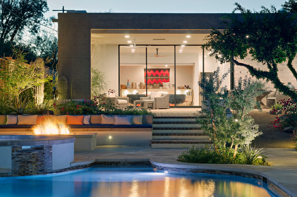 Réalisation d'une terrasse arrière minimaliste de taille moyenne avec un foyer extérieur, des pavés en pierre naturelle et une extension de toiture.