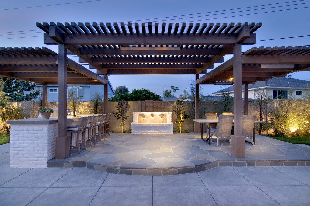 Large classic back patio in Orange County with an outdoor kitchen, natural stone paving and a pergola.