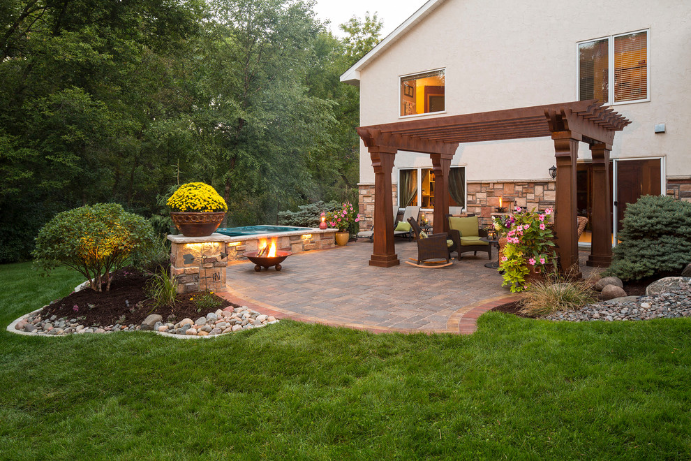Modelo de patio tradicional de tamaño medio en patio trasero con adoquines de piedra natural, brasero y pérgola
