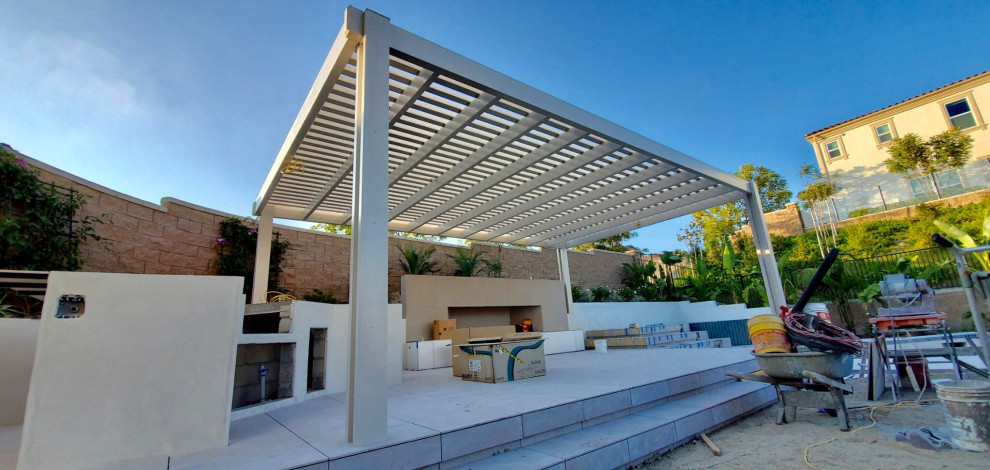 This is an example of a large modern back patio with an outdoor kitchen, tiled flooring and a pergola.