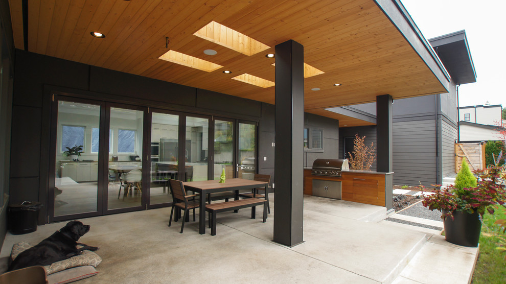 Cette image montre une grande terrasse minimaliste avec une cour, une extension de toiture, une cuisine d'été et une dalle de béton.
