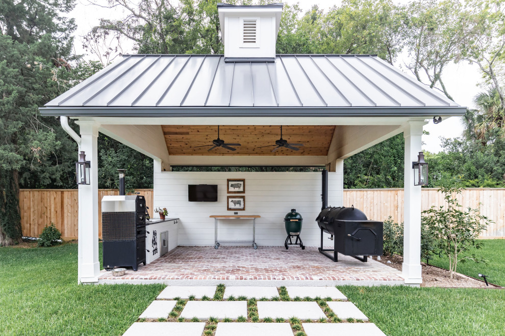 Modelo de patio de estilo de casa de campo de tamaño medio en patio trasero con cocina exterior, adoquines de ladrillo y cenador