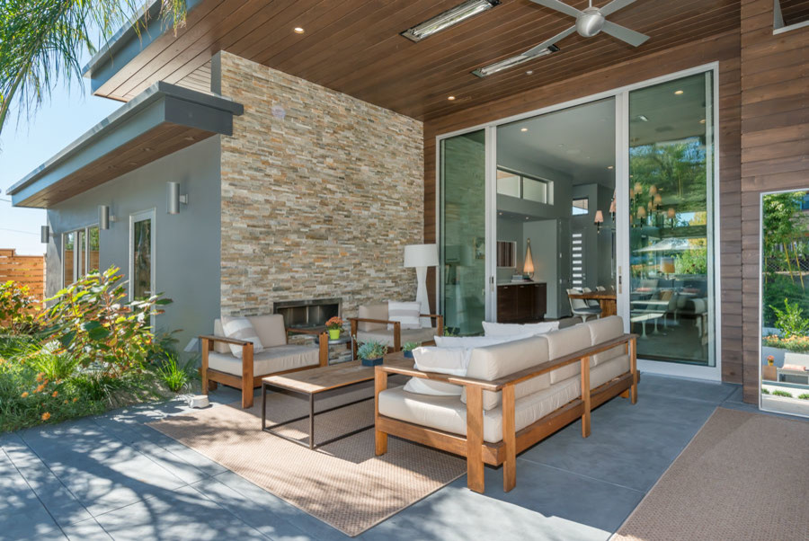 Immagine di un patio o portico minimalista di medie dimensioni e dietro casa con un focolare, lastre di cemento e un tetto a sbalzo