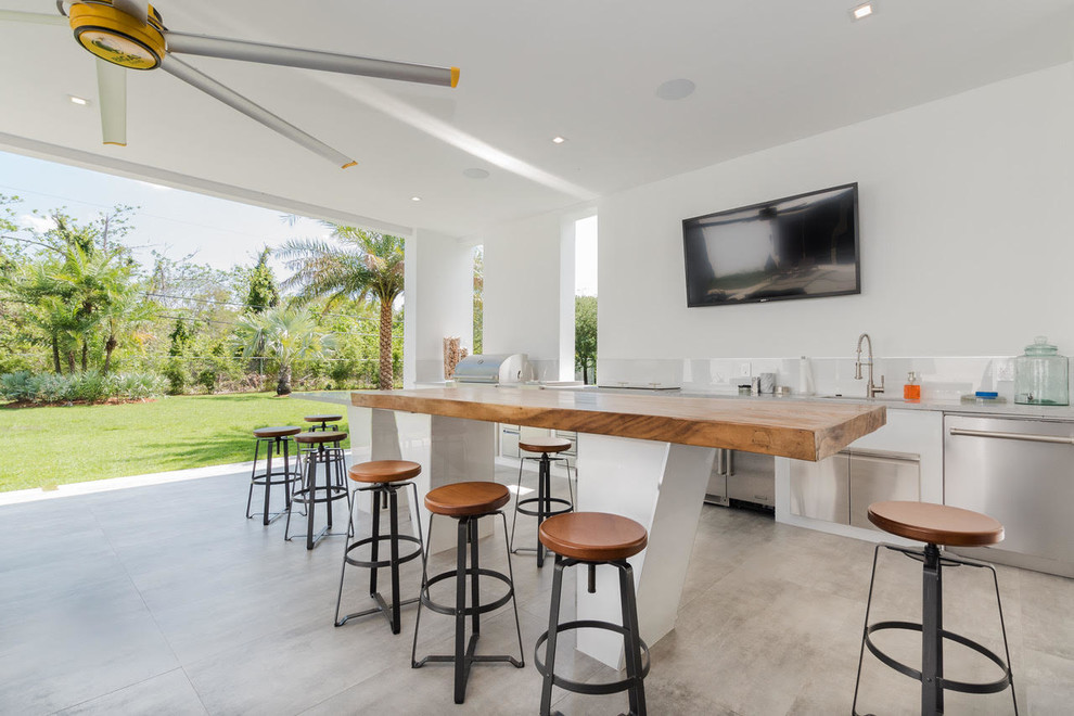 Example of a large minimalist backyard concrete paver patio kitchen design in Miami with a roof extension